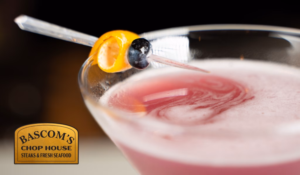 Close-up of a pink cocktail with an orange twist and berry garnish at Bascom’s Chop House